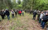 Uczestnicy konferencji na sesji terenowej w lesie, stoją w okręgi i dyskutują na temat lasu