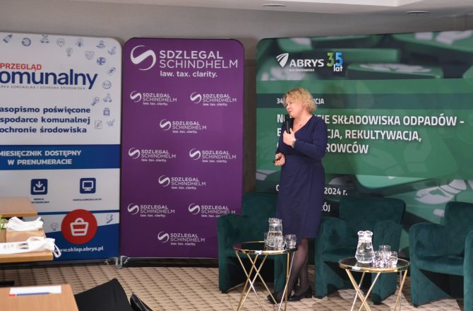 Prof. Justyna Jurczyk stoi przed banerami konferencji ze wskaźnikiem w ręku