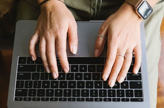 Dłonie piszące na klawiaturze laptopa.